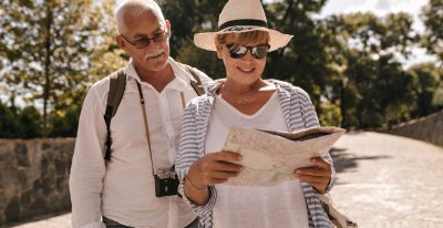 blonde-woman-white-t-shirt-blue-blouse-sunglasses-hat-smiling-looking-map-lady-walks-with-mustachioed-man-shirt-with-camera-outdoor-scaled.jpg
